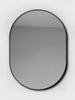 Oval-shaped mirror with a black aluminum frame, hanging on a white background